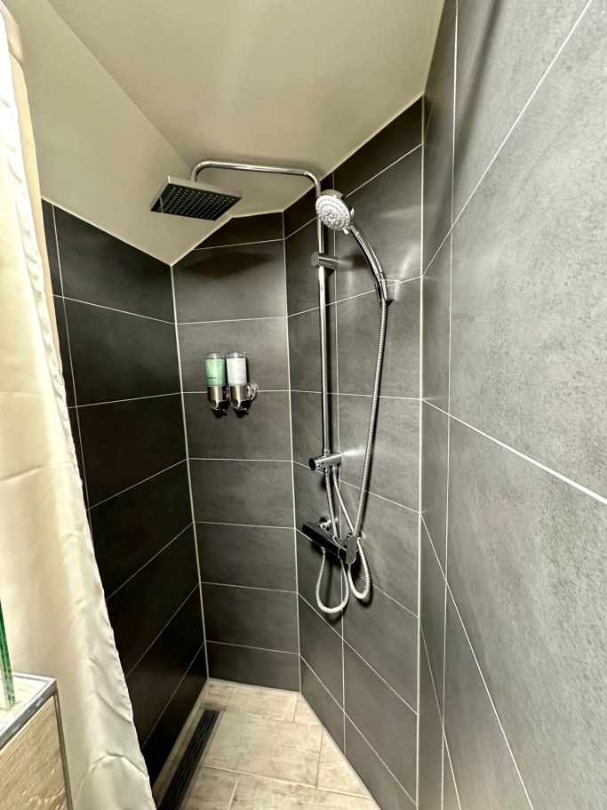 Bathroom 2 with smart toilet A&A Patio suite queen room toilet 2. Moderne douche met zwarte tegels, regendouche en wandbeugels voor shampoo en zeep.