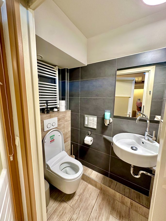 Bathroom 2 with smart toilet A&A Patio suite toilet 2. Kleine, moderne badkamer met een toilet en wastafel naast een spiegel.