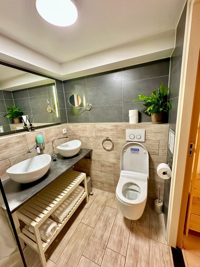 Bathroom 1 with smart toilet A&A Patio suite queen room toilet. Moderne badkamer met twee wastafels, toilet en planten op de plank.