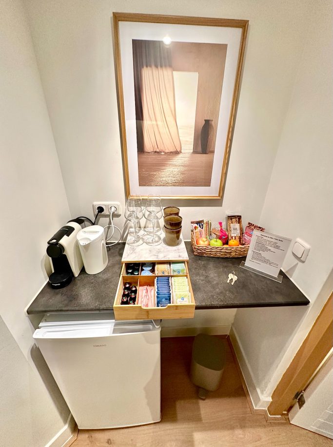 Complimentary Refreshments Area A&A PAtio suite queen room minibar. Klein bureau met koffiemachine, glazen, kleurrijke snacks en een koelkastje.